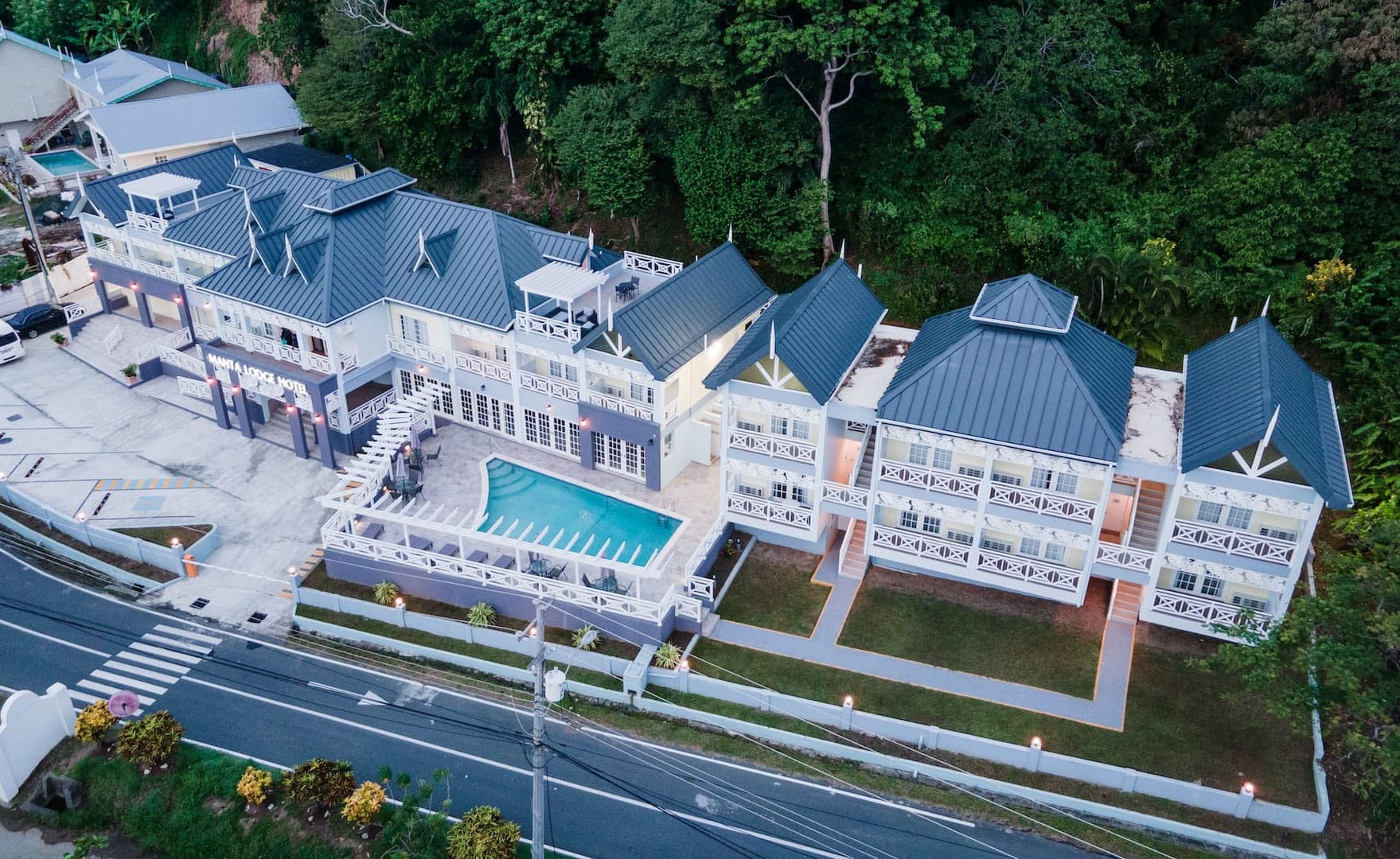 Aerial view of a large, multi-story building with a pool in the courtyard, surrounded by lush greenery and situated near a road.